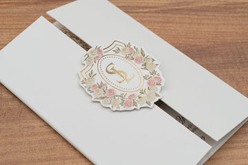 Elegant white wedding invitation with gold monogram and floral crest on wooden table
