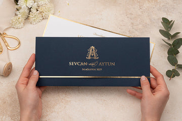 Elegant navy blue wedding invitation with gold foil accents, held by hands on marble surface.