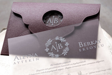 Elegant wedding invitation with floral monogram and purple envelope on a neutral background