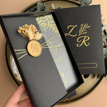 Elegant black and gold wedding invitation with wax seal and dried floral accents in a premium box.