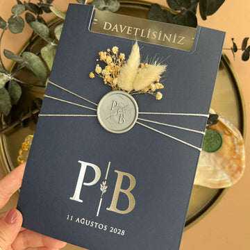 Elegant navy blue wedding invitation with wax seal, silver initials, and dried floral accents