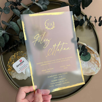 Elegant gold foil wedding invitation with translucent acrylic design, held by hand, greenery decor